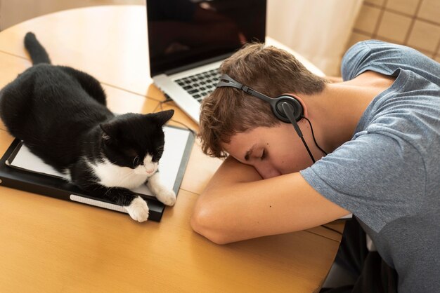 Uomo stanco con gatto che lavora a casa durante la quarantena