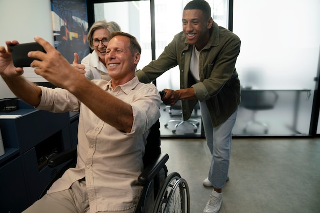 Uomo su sedia a rotelle che si fa un selfie sul posto di lavoro con i colleghi