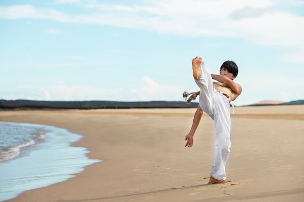 Uomo sulla spiaggia che pratica capoeira da solo