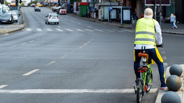 Uomo sulla strada su una piccola bicicletta verde, strada con auto e persone