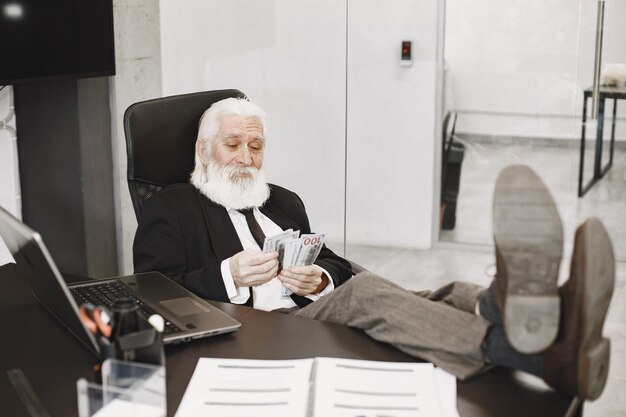 Uomo vecchio stile seduto al tavolo. Uomo elegante in ufficio. Anziano con un denaro.