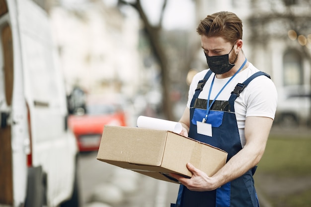 Uomo vicino al camion. Ragazzo in uniforme da consegna. Uomo in una maschera medica. Concetto di coronavirus.