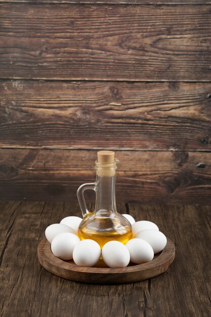 Uova bianche crude e bottiglia di olio d'oliva sulla tavola di legno.