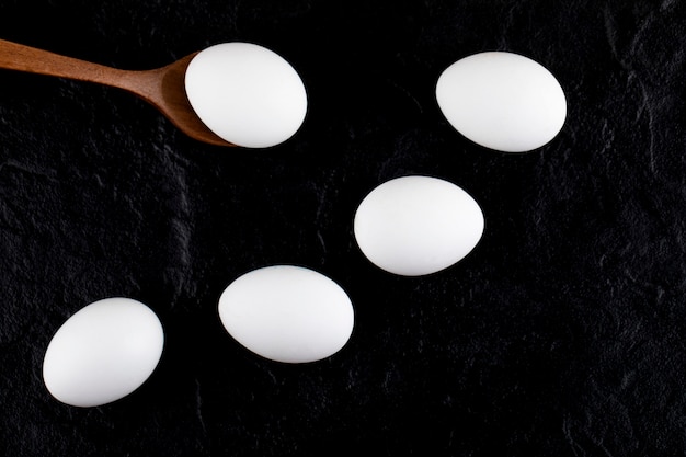 Uova bianche crude e cucchiaio di legno sulla superficie nera.