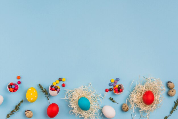 Uova colorate nei nidi con piccole caramelle sul tavolo