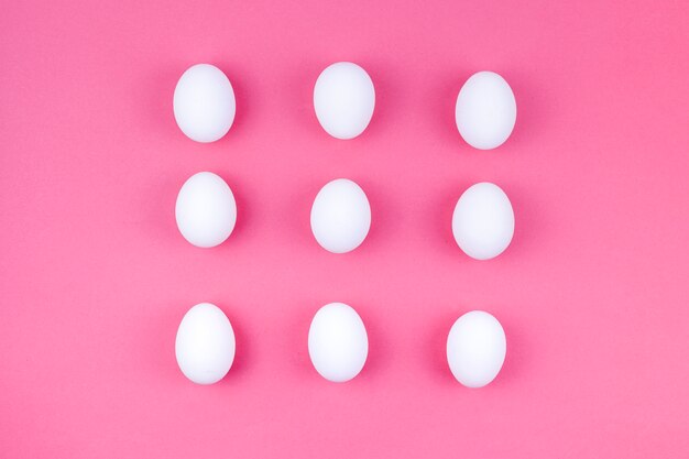 Uova di gallina bianca sparse sul tavolo rosa