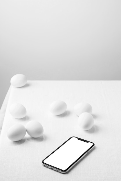 Uova di gallina bianche ad alto angolo sul tavolo con telefono vuoto