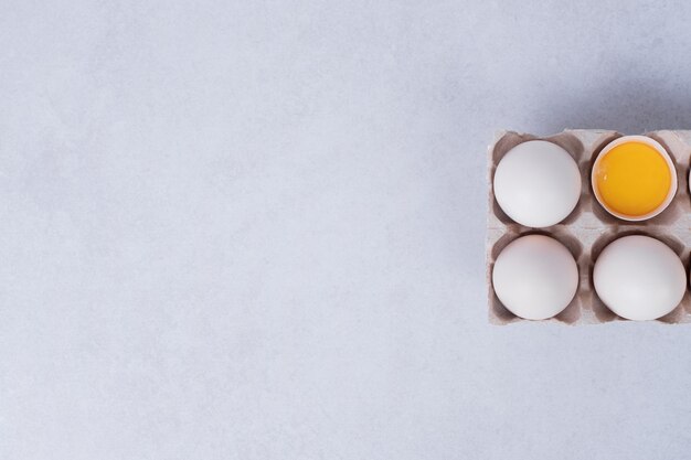 Uova di gallina in un contenitore di carta sulla superficie bianca.