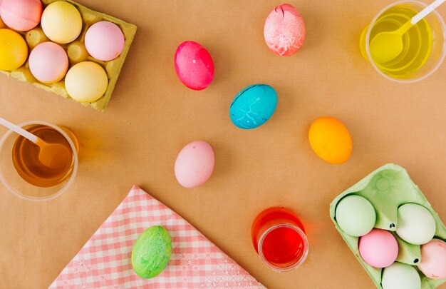 Uova di Pasqua in contenitori vicino a tazze con liquido colorante e tovagliolo colorato