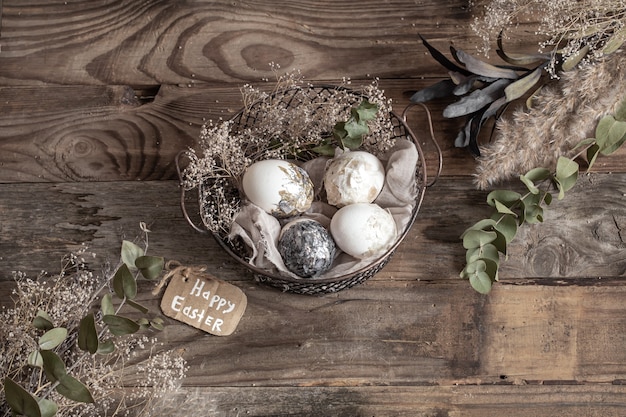 Uova di Pasqua in un cesto decorativo con fiori secchi su un tavolo di legno. Felice Pasqua concetto.