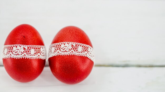 Uova di Pasqua rosse su un bianco legate con un nastro di pizzo, primo piano, sdraiato su un legno bianco