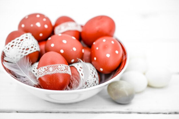 Uova di Pasqua rosse su un piatto bianco e sul nastro di pizzo legato bianco, primo piano