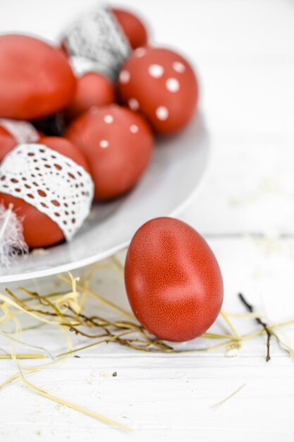 Uova di Pasqua rosse su un piatto bianco e sul nastro di pizzo legato bianco, primo piano