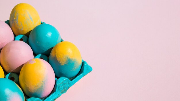 Uova di Pasqua variopinte in cremagliera blu sulla tavola rosa