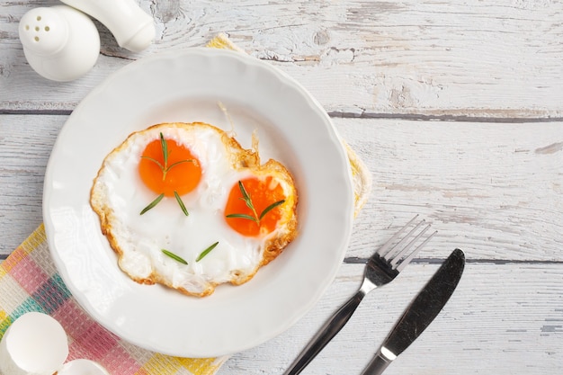 Uova fritte in un piatto bianco su superficie di legno bianca