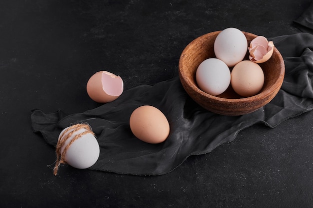 Uova in una tazza di legno su un canovaccio da cucina nero.