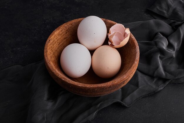 Uova in una tazza di legno su un canovaccio da cucina nero.