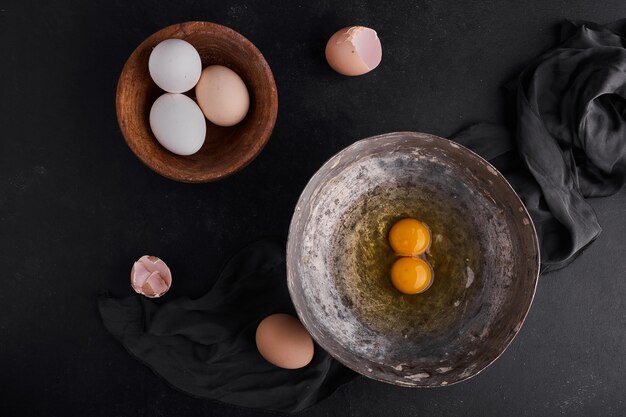 Uova intere e tuorli in piatti di legno e metallici, vista dall'alto.