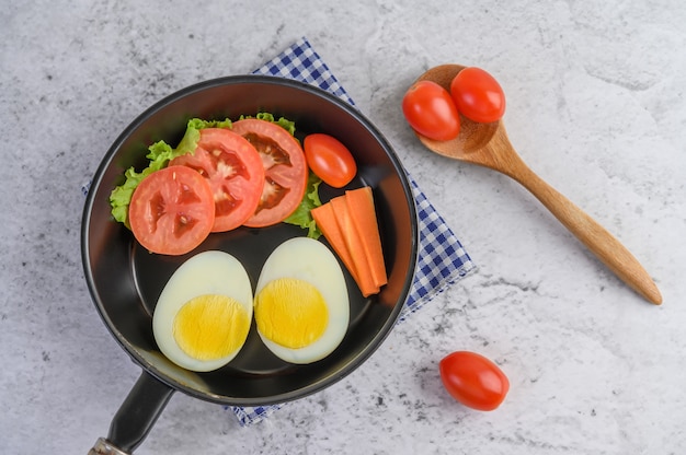 Uova sode, carote e pomodori su una padella con il pomodoro su un cucchiaio di legno.