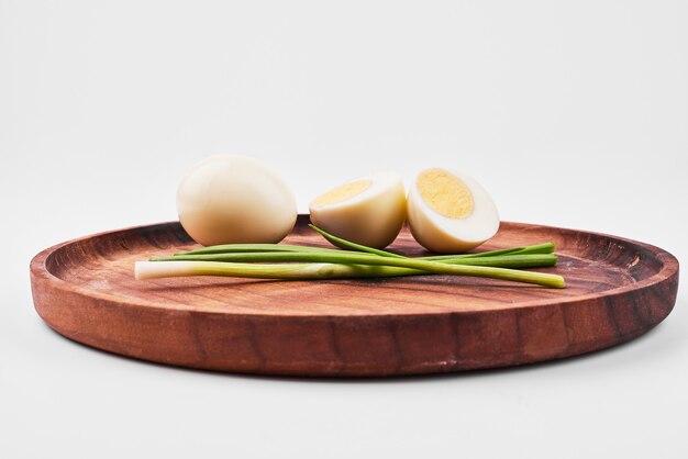 Uova sode e cipolla verde sul piatto di legno.