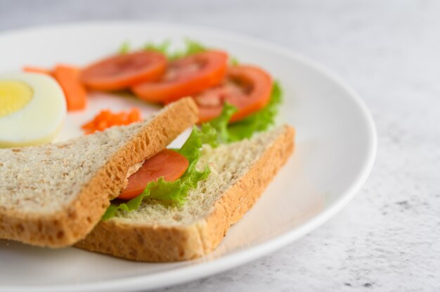 Uova sode, pane, carote e pomodori su un piatto bianco con un coltello e una forchetta.