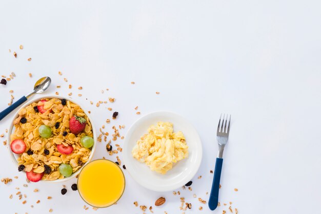 Uova strapazzate; bicchiere di succo e cornflakes con frutta secca su sfondo bianco