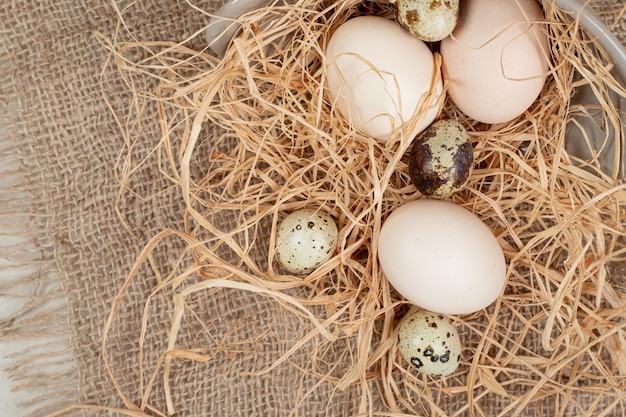 Uovo di gallina con uova di quaglia e fieno su tela di sacco.