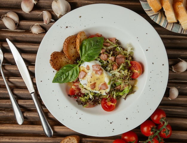 Uovo fritto di vista superiore in un piatto bianco con insalata verde