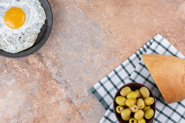 Uovo fritto in padella servito con olive verdi marinate