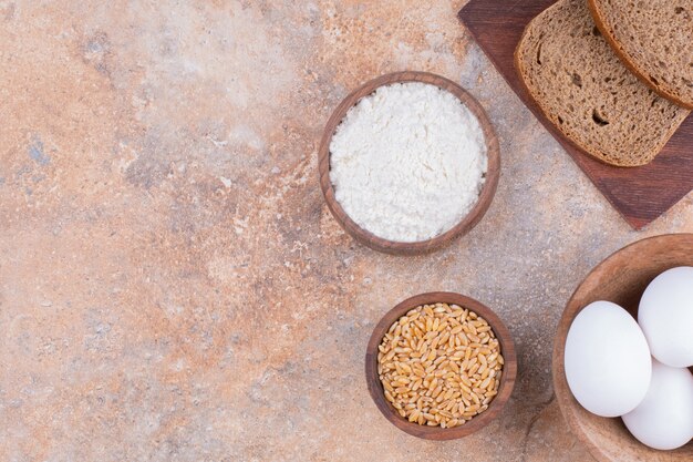 Uovo, grano, farina e pane a fette su una tavola, sul marmo.