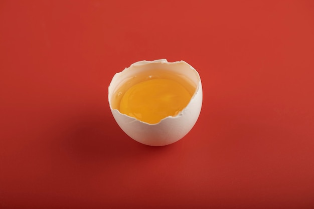 Uovo organico rotto sulla superficie rossa.