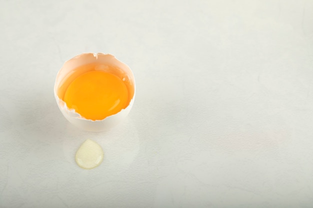 Uovo rotto crudo su superficie bianca.