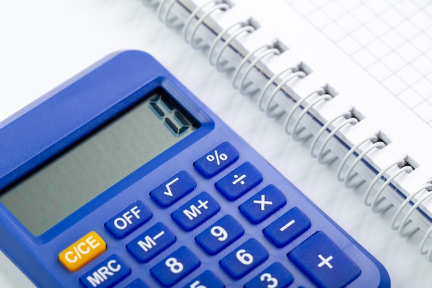Uso blu della mano di contabilità di sguardo più vicino del calcolatore con il quaderno bianco sullo scrittorio bianco
