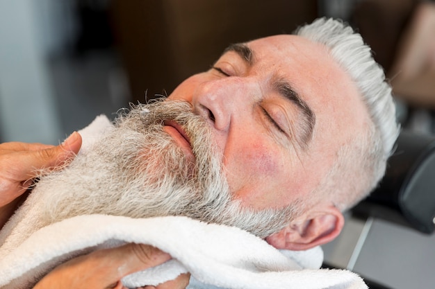 Utilizzando un asciugamano sulla barba del maschio invecchiato nel negozio di barbiere