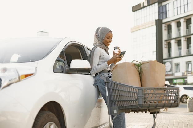 Utilizzo dello smartphone durante l'attesa. Donna di etnia africana sulla stazione di ricarica delle auto elettriche durante il giorno