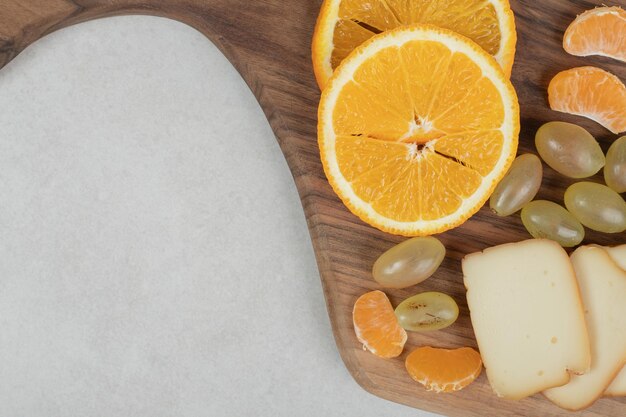Uva, arance, mandarini e formaggio su tavola di legno.