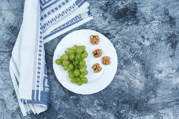 Uva bianca piatta laici, noci nel piatto bianco con carta da cucina su sfondo di marmo blu scuro. orizzontale