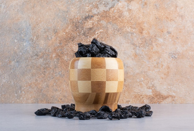 Uva passa nera in una tazza di legno su fondo di cemento.