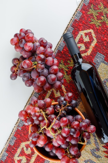 Uva rossa in una ciotola con vista dall'alto di vino sul tappeto bianco e tradizionale