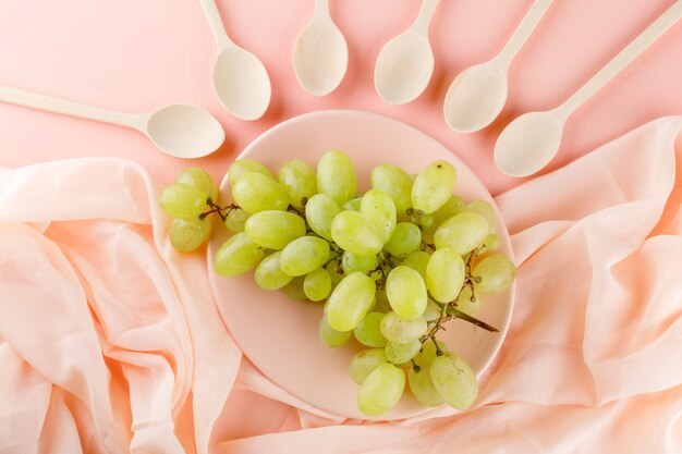 Uva verde con cucchiai di legno in un piatto su rosa e tessuto,