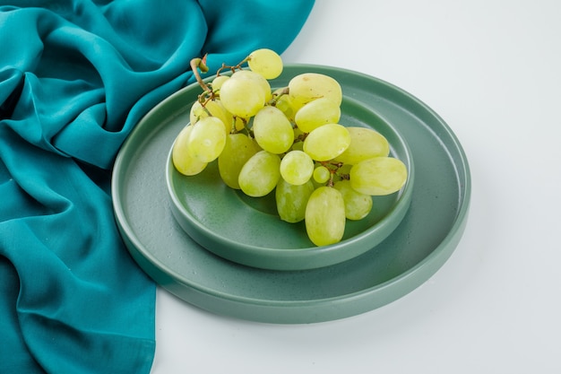 Uva verde in un piattino con vista dall'alto angolo piatto su bianco e tessile