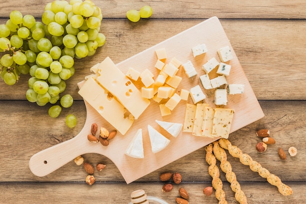 Uva verde, mandorle, grissini e blocchi di formaggio sul tagliere sulla scrivania in legno