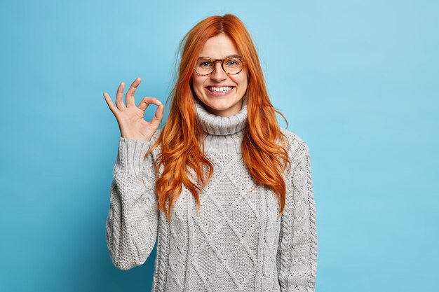 Va bene, va bene. La donna sorridente dello zenzero fa un ottimo segno completamente d'accordo con il tuo suggerimento approva qualcosa vestito con un maglione grigio.