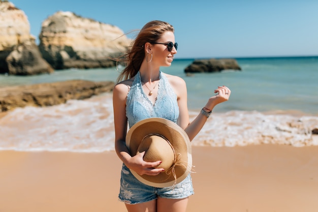 Vacanza al mare. Bella donna in cappello da sole godendo perfetta giornata di sole camminando sulla spiaggia. Felicità e beatitudine.