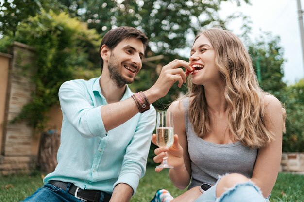 Vacanze estive, persone, romanticismo, uomo e donna che si alimentano a vicenda fragole bevendo frizzante e godendosi il tempo insieme a casa