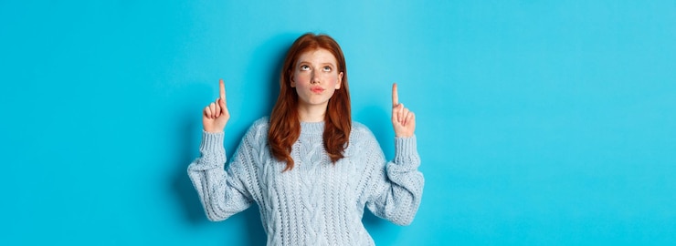 Foto gratuito vacanze invernali e concetto di persone ragazza rossa premurosa in maglione che fissa e punta le dita u