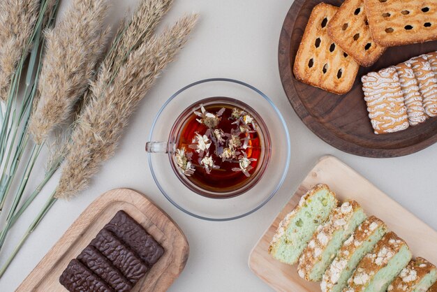 Vari biscotti, fette di torta e tazza di tè su bianco.