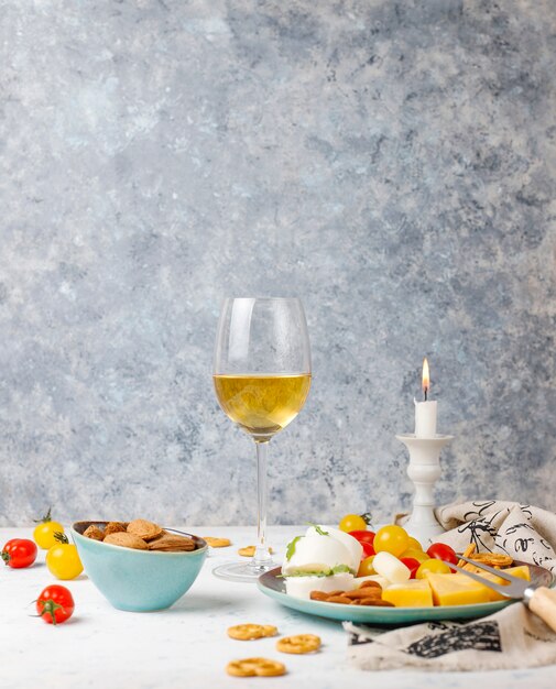 Vari formaggi e piatto di formaggi sul tavolo luminoso con diversi tipi di noci e frutta e bicchiere di vino
