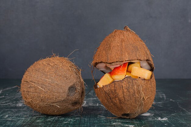 Vari frutti in noce di cocco tagliata a metà con paglia sul tavolo di marmo