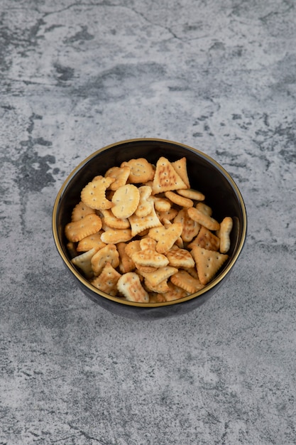 Vari piccoli cracker in ciotola nera su sfondo marmo.